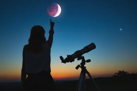 Estos son los signos del Zodíaco más favorecidos por el eclipse del 17 de septiembre Una mujer con un telescopio mirando una luna eclipsada.