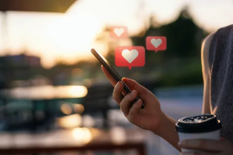 ¿Qué es el breadcrumbing y por qué es el nuevo boom en las apps de citas? Una mano sosteniendo un celular del que salen corazones.
