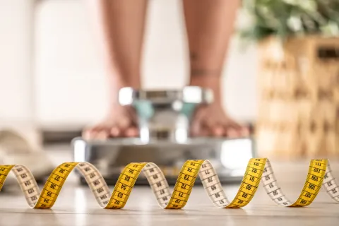 Día Internacional de Lucha contra los TCA: "Soy mamá de una adolescente con un trastorno de alimentación" Los pies de una mujer sobre una balaza y un centímetro en primer plano.