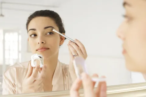 Makeup fake: por qué hay que evitar comprar maquillaje de imitación, según una experta Una mujer maquillándose frente al espejo