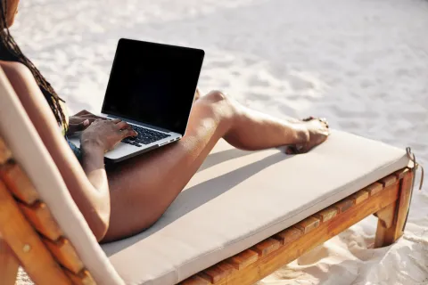 Una mujer en la playa con una laptop sobre las piernas.