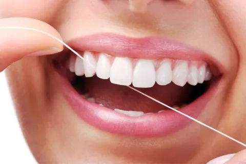 Estas son las 3 patologías que más deterioran tus dientes y cómo tratarlas mujer sonrie y se pasa el hilo dental