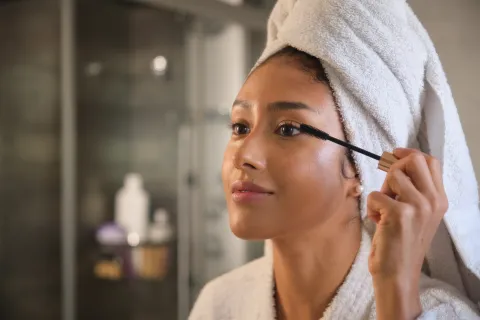 Cinco consejos para cuidar y fortalecer tus pestañas naturales Foto de mujer peinandose las pestañas.