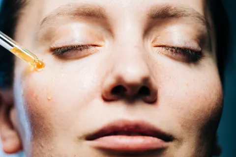 Hola invierno: ¿por qué hablamos de renovación de la piel cuando llega el frío? una mujer con un gotero aplicandose un serum en el rostro