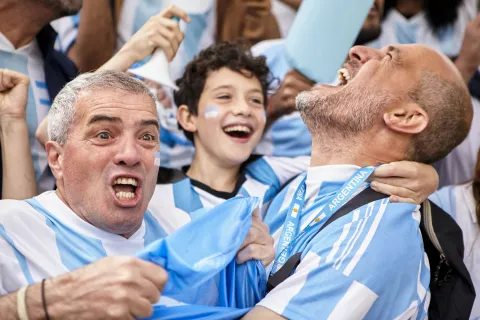 dos hombres y un nene hinchando por argentina emocionados en un partido de futbol