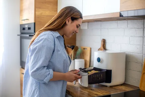 Estos son los electrodomésticos que consumen más energía eléctrica (y quizás no lo sabías) Freidora de aire y una mujer en la cocina