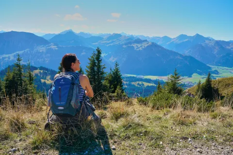Feriado del 12 de octubre: 6 destinos para armar una escapada corta en este finde largo Mujer sentada con una mochila en los hombros contemplando el paisaje montañoso.