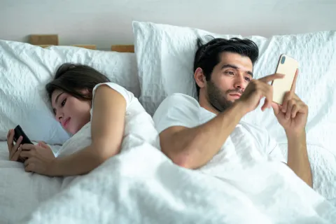 Recesión sexual: por qué cada vez tenemos menos sexo, menos citas y menos ganas de enamorarnos pareja en cama con celular