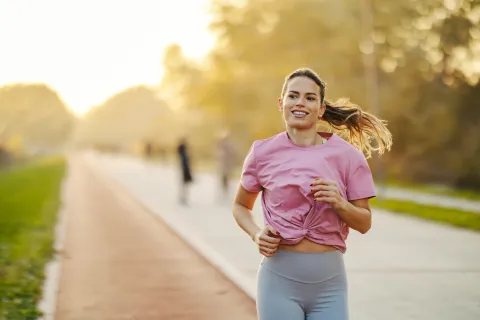 Cómo retomar el running al aire libre después del invierno sin lesionarte en el intento Mujer corriendo por un camino arbolado