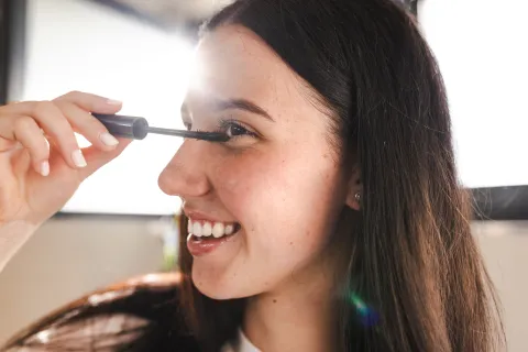 Una mujer pintándose las pestañas con una máscara frente al espejo