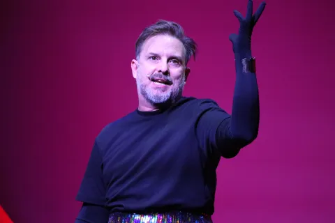 Juan Pablo Geretto y el regreso de "Solo como una perra": “El humor es una herramienta de supervivencia” Juan Pablo Geretto levantando un brazo, vestido de negro.