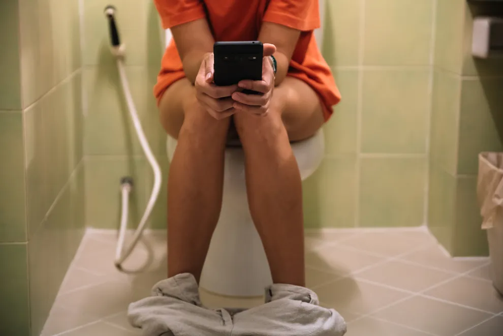 Una mujer sentada en el inodoro con un celular en la mano.